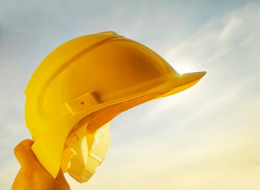 Güneşli arka planda sarı miğfer tutan mühendis. Güneş ışığı. güneş ışınları.