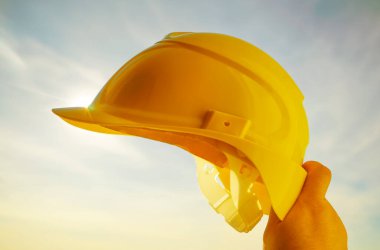 Güneşli arka planda sarı miğfer tutan mühendis. Güneş ışığı. güneş ışınları.