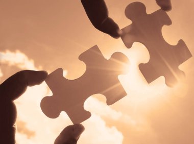 Gökyüzü arka planında yapboz parçaları olan eller.  