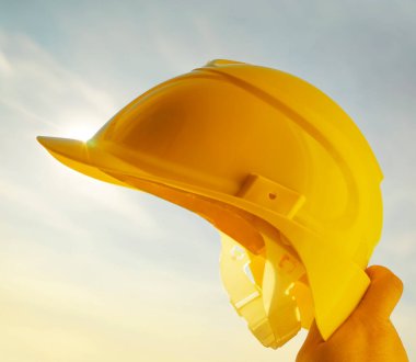 Güneşli arka planda sarı miğfer tutan mühendis. Güneş ışığı. güneş ışınları.