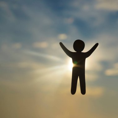 Gün batımında gökyüzü arka planında elleri havada insan figürünün silüeti.