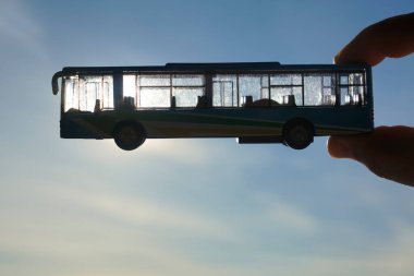 Gökyüzünün arka planına karşı erkek eli üzerinde mavi bir otobüsün oyuncak modeli. Ulaşım kavramı 