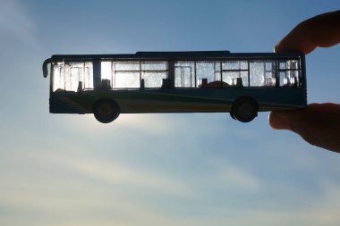 Gökyüzünün arka planına karşı erkek eli üzerinde mavi bir otobüsün oyuncak modeli. Ulaşım kavramı 