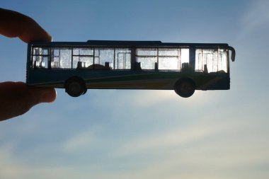 Gökyüzünün arka planına karşı erkek eli üzerinde mavi bir otobüsün oyuncak modeli. Ulaşım kavramı 