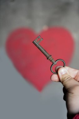 Erkek el, duvarın arkasında kırmızı kalpli eski bir anahtar tutuyor..