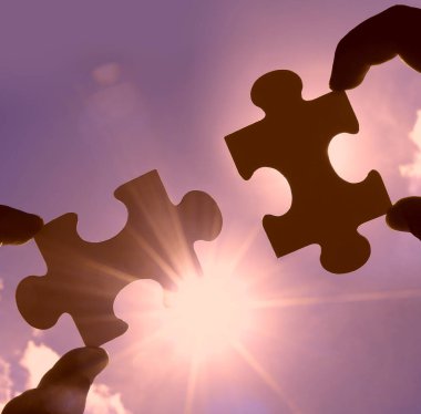 Gökyüzü arka planında yapboz parçaları olan eller.  