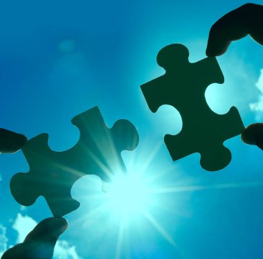 Gökyüzü arka planında yapboz parçaları olan eller.  