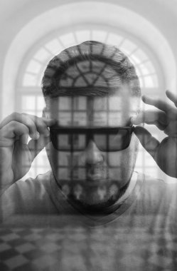 Modern yuvarlak siyah gözlük takan yakışıklı genç adam pencere çerçevesinin arkasına bakıyor. çift pozlama.