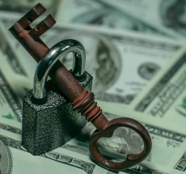 Iron lock key on the group of money stack of 100 US dollars banknote a lot of the background texture, top view.