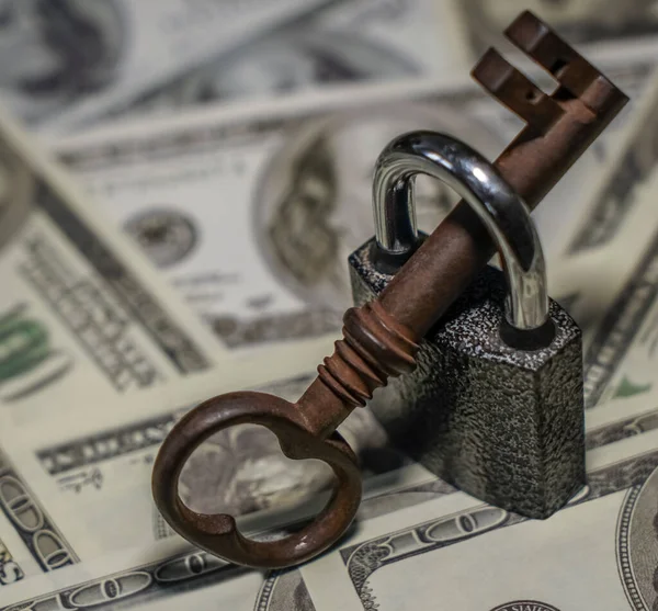 Iron lock key on the group of money stack of 100 US dollars banknote a lot of the background texture, top view.