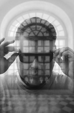 Modern yuvarlak siyah gözlük takan yakışıklı genç adam pencere çerçevesinin arkasına bakıyor. çift pozlama.