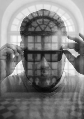 Modern yuvarlak siyah gözlük takan yakışıklı genç adam pencere çerçevesinin arkasına bakıyor. çift pozlama.