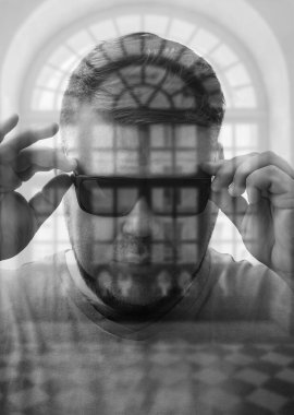 Modern yuvarlak siyah gözlük takan yakışıklı genç adam pencere çerçevesinin arkasına bakıyor. çift pozlama.