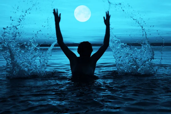 Black silhouette of woman. splashing water above head.  summer vacation. holiday active.  blue sea and sunset sky. Healthy happiness lifestyle. hands up. full moon in the sky.