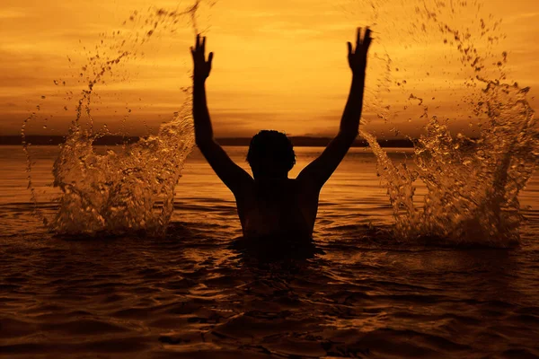 Black silhouette of woman. splashing water above head.  summer vacation. holiday active.  yellow sea and sunset sky. Healthy happiness lifestyle. hands up