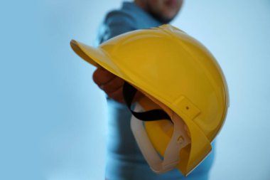 Sarı kasklı bir erkek el. İnsan El, mavi arka planda izole edilmiş bir şapka tutuyor. Yüzü yok. 