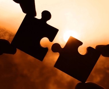 Gökyüzü arka planında yapboz parçaları olan eller.  