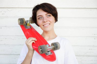 Young woman holding red skateboard on shoulder isolated on  white wall background