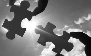 Gökyüzü arka planında yapboz parçaları olan eller.  