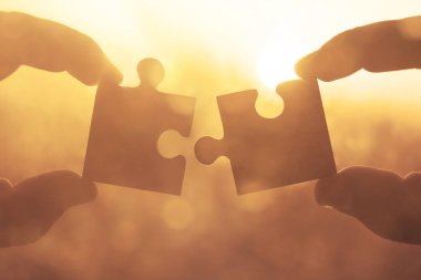 Gökyüzü arka planında yapboz parçaları olan eller.  