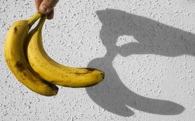 Erkek elinde sarı muzlar. Arka planda beyaz beton duvar var. Çitin üzerinde güneş ışığı ve gölge. 