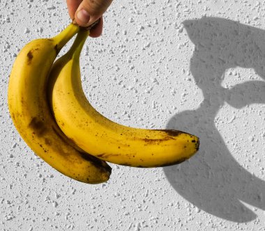 Erkek elinde sarı muzlar. Arka planda beyaz beton duvar var. Çitin üzerinde güneş ışığı ve gölge. 