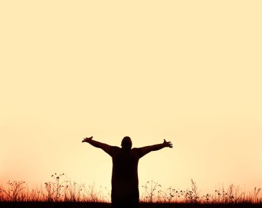 Vahşi tarlada günbatımının arka planında ellerini kaldırmış genç bir adamın silueti. 
