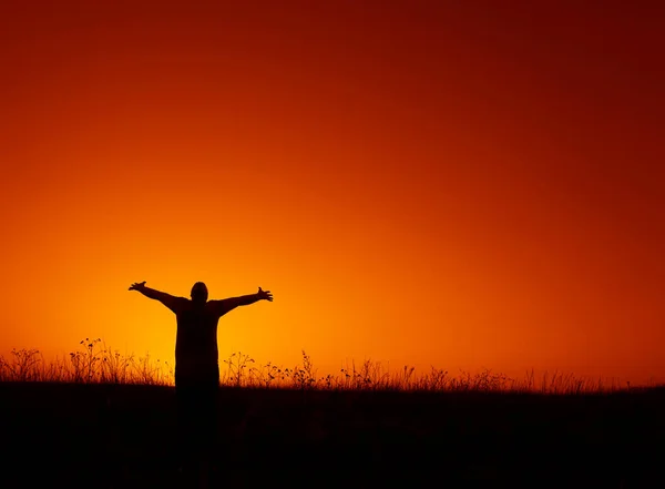Silhouette of a young man with hands up against the background of the sunset in wild field. Silhouette of Man Raising His Hands or Open arms  with sunset, sunlight. freedom concept.
