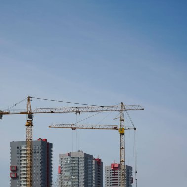 Yüksek binaların ve mavi gökyüzünün arka planında inşaat vinçleri kapanıyor. Yükselen vinç, mavi gökyüzüne karşı beton bir plaka kaldırıyor.. 