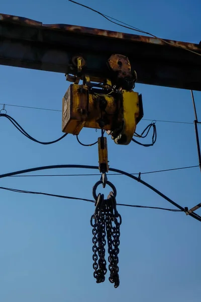 Hook gantry crane on the chain for lifting heavy loads on the background of a metal beam and a blue sky.