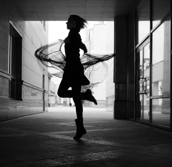 woman dances to the music in the city. silhouette of girl dancing between walls.