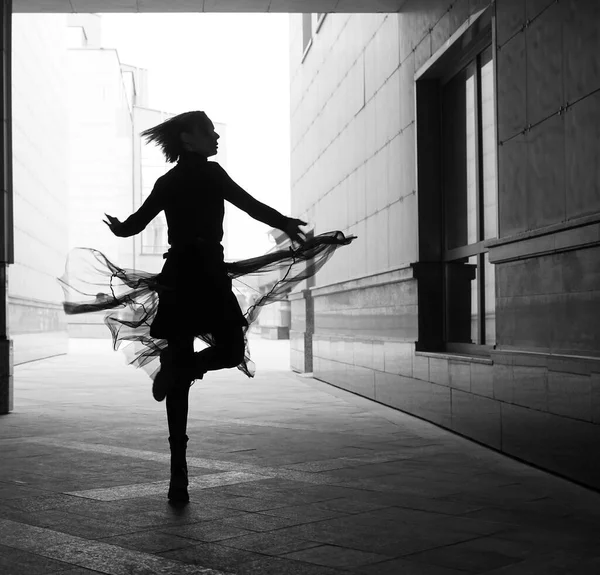 woman dances to the music in the city. silhouette of girl dancing between walls.