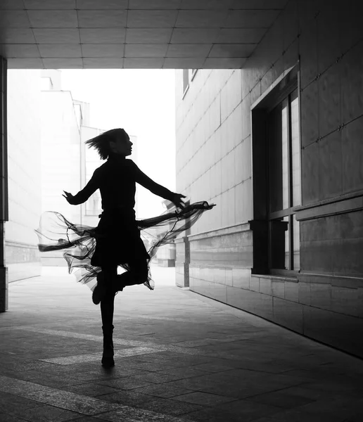 woman dances to the music in the city. silhouette of girl dancing between walls.