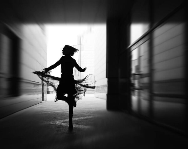 Woman dances to the music in the city. silhouette of girl dancing between walls.