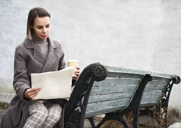 成熟的女商人坐在老化的木制长椅上休息 喝咖啡和看报 — 图库照片