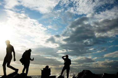 Turistlerin silueti fotoğraf çekiyor. Cep telefonu kullanan genç bir kadının yan görüntüsü. Denizin fotoğraflarını çek.
