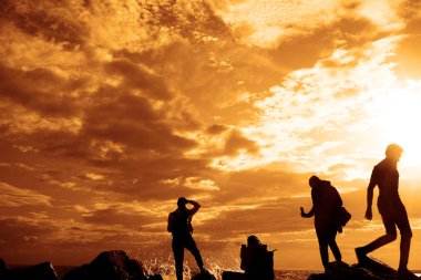 Turistlerin silueti fotoğraf çekiyor. Cep telefonu kullanan genç bir kadının yan görüntüsü. Denizin fotoğraflarını çek.