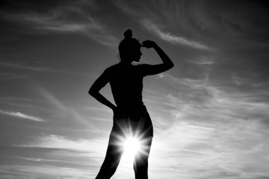 Kadın silueti. Altın saat. Arka planda alacakaranlık ışıkları. Yaşam tarzı ve günbatımı. Kadın gökyüzünde duruyor. Kız uzaklara bakıyor.