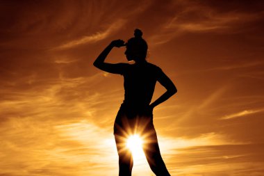 Kadın silueti. Altın saat. Arka planda alacakaranlık ışıkları. Yaşam tarzı ve günbatımı. Kadın gökyüzünde duruyor. Kız uzaklara bakıyor.