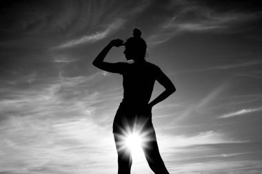 Kadın silueti. Altın saat. Arka planda alacakaranlık ışıkları. Yaşam tarzı ve günbatımı. Kadın gökyüzünde duruyor. Kız uzaklara bakıyor.