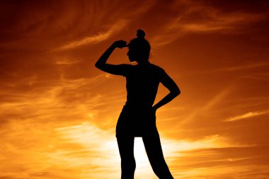 Kadın silueti. Altın saat. Arka planda alacakaranlık ışıkları. Yaşam tarzı ve günbatımı. Kadın gökyüzünde duruyor. Kız uzaklara bakıyor.