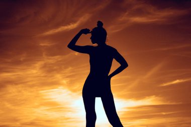 Kadın silueti. Altın saat. Arka planda alacakaranlık ışıkları. Yaşam tarzı ve günbatımı. Kadın gökyüzünde duruyor. Kız uzaklara bakıyor.