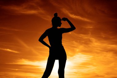 Kadın silueti. Altın saat. Arka planda alacakaranlık ışıkları. Yaşam tarzı ve günbatımı. Kadın gökyüzünde duruyor. Kız uzaklara bakıyor.