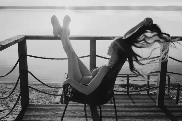 长发姑娘坐在扶手椅上 在阳台上晒日光浴 背景是海景 — 图库照片