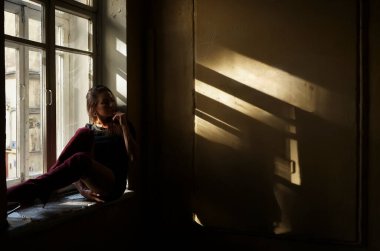 Uzun saçlı, rüya gören bir kadın pencere eşiğinde oturur..