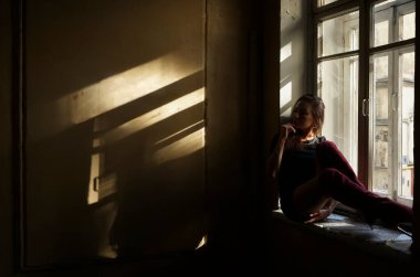 Uzun saçlı, rüya gören bir kadın pencere eşiğinde oturur..