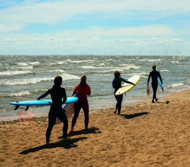 Arkadaşlık, deniz, yaz tatili, su sporları ve insanların konsepti. Sahilde sörf tahtalı mayo giyen bir grup arkadaş. arka plan
