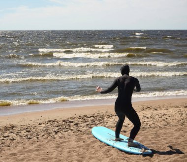 Güneşli bir günde kumlu sahilde sörf tahtasında uzanan dalgıç kıyafetli bir kadın. Isınma turu. arka plan.