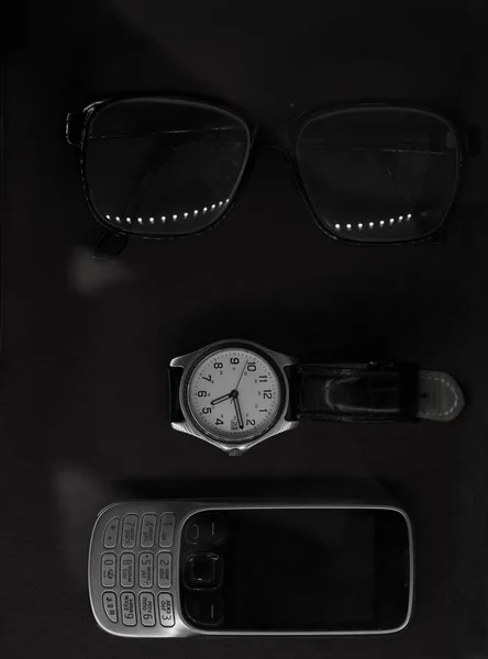 glasses , retro mobile phone and watch lie on black tablecloth. Black and white composition. Flat lay.