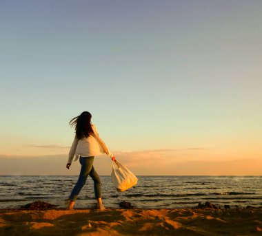 Rüzgarlı saçlı ve çantalı şık bir kadın kumlu sahilden denize yürüyor, tasasız bir an. Beyaz gömlekli şık bir bayan tatilin tadını çıkarıyor ve sahilde dinleniyor. Boşluğu kopyala